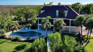 Une maison à deux étages avec une piscine, entourée de palmiers et de verdure.