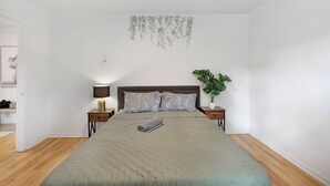 Un dormitorio con cama, mesitas de noche, una lámpara y una planta en maceta.