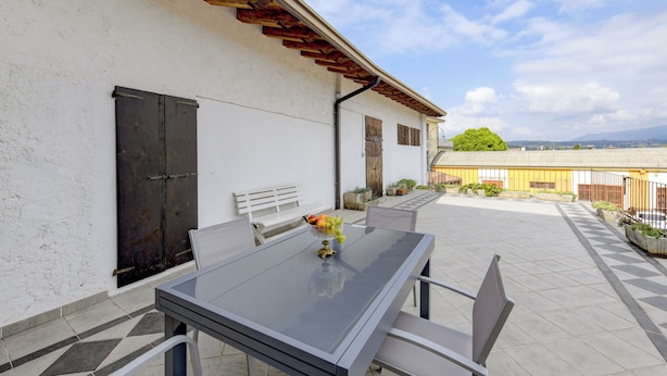 Een terras buiten met een glazen tafel, stoelen, een bank en potplanten.