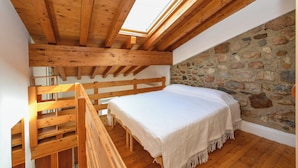 Een slaapkamer met een houten plafond, dakraam, stenen muur en een bed met een witte dekbedovertrek.