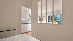 Une chambre avec une grande fenêtre, un lit et une vue sur la cuisine et l’espace extérieur.