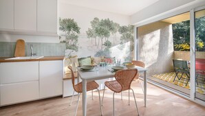 Une cuisine moderne avec un coin repas, dotée d’une grande fenêtre offrant une vue sur les arbres et donnant sur un patio.