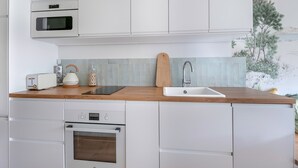 Une cuisine moderne avec des meubles blancs, un plan de travail en bois, un four encastré, un grille-pain et un évier.
