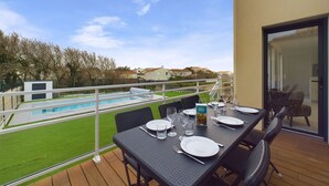 A balcony with a dining table set for two, overlooking a swimming pool and a grassy area with houses in the background. - 350m from the beach, house for 7 with a pool (Bretignolles-sur-Mer)