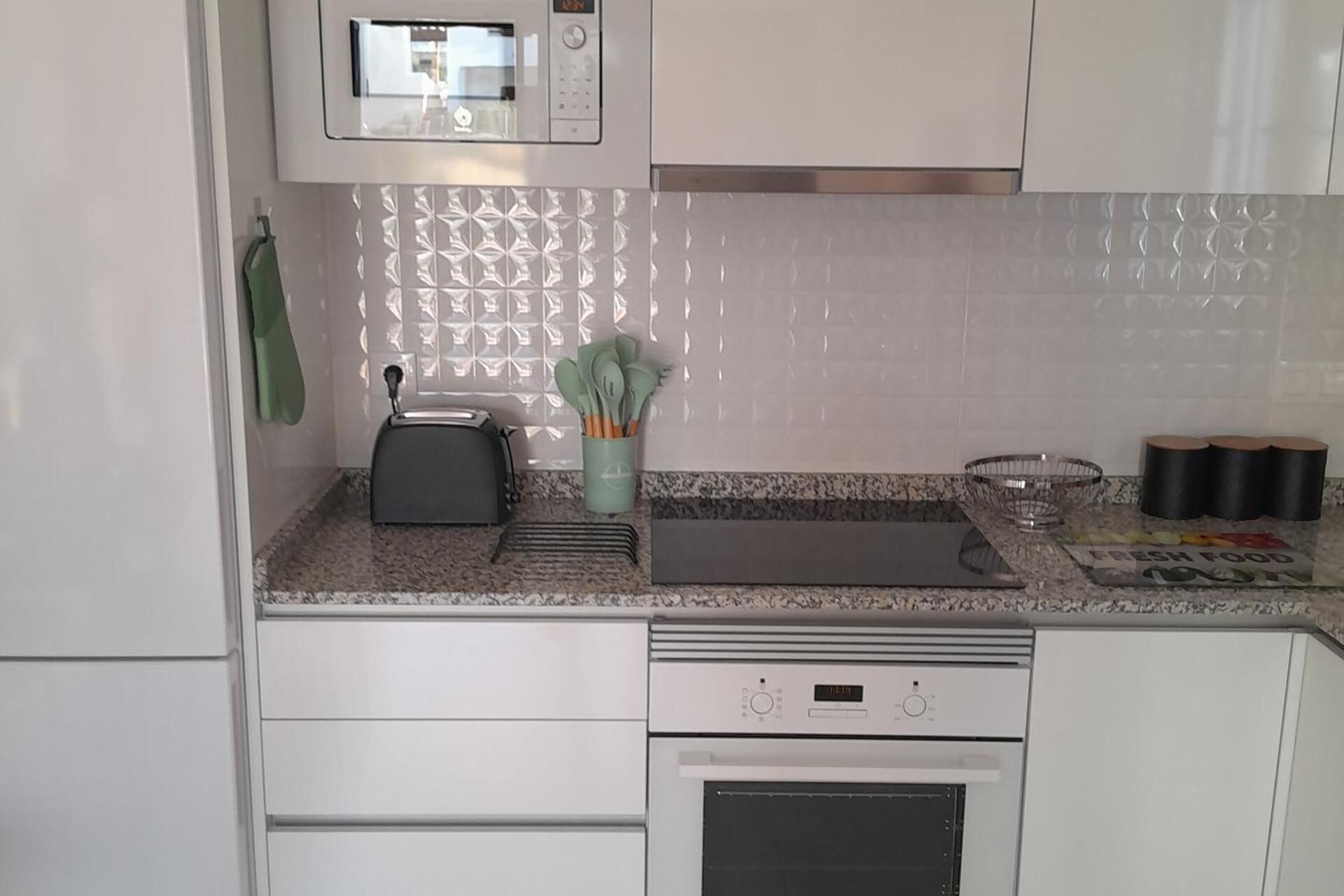 A kitchen with white cabinets, a microwave, a toaster, a cutting board, a bowl, and a roll of tape.