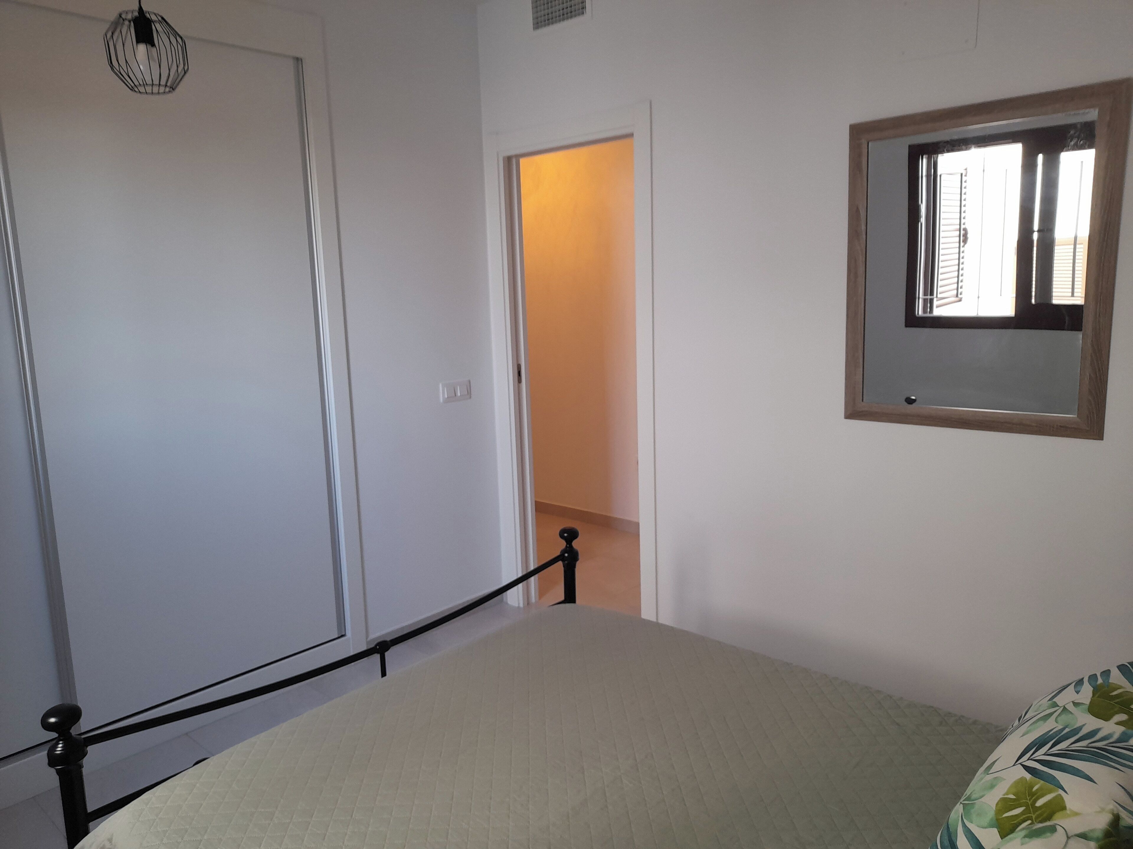 A bedroom with a bed, a window with blinds, a door, and a light fixture.