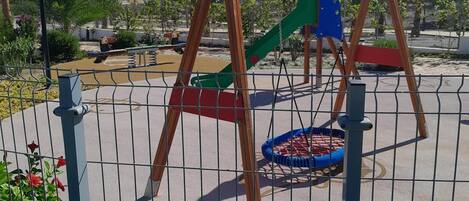 Ein Spielplatz mit Schaukeln, Rutschen und einem eingezäunten Bereich.