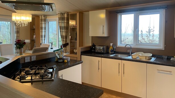 A modern kitchen with a gas stove, white cabinets, a window with a view, and a chandelier. - Lilac Lodge Retreat for 6, Set in One Acre of Land (Otley)