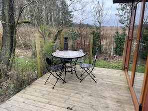 An outdoor wooden deck with a round table and chairs, surrounded by trees and vegetation. - Lilac Lodge Retreat for 6, Set in One Acre of Land (Otley)
