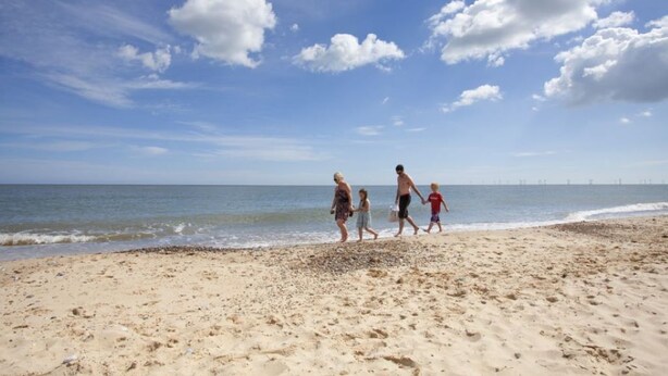 A sandy beach with footprints, a clear sky, and a calm sea.
