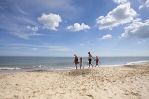 Une plage de sable parsemée d’empreintes, un ciel dégagé et une mer calme.