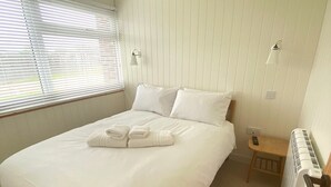 A neatly made bed with white linens and towels, a small bedside table with a lamp, and a radiator on the wall.