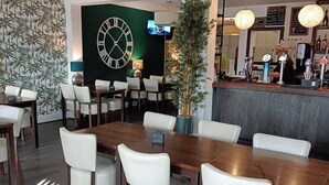 A modern dining area with wooden tables and white chairs, a large wall clock, and a bar counter with a bartender.