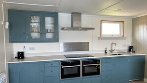 A modern kitchen with blue cabinets, a stainless steel range hood, a built-in oven, and a window above the sink.