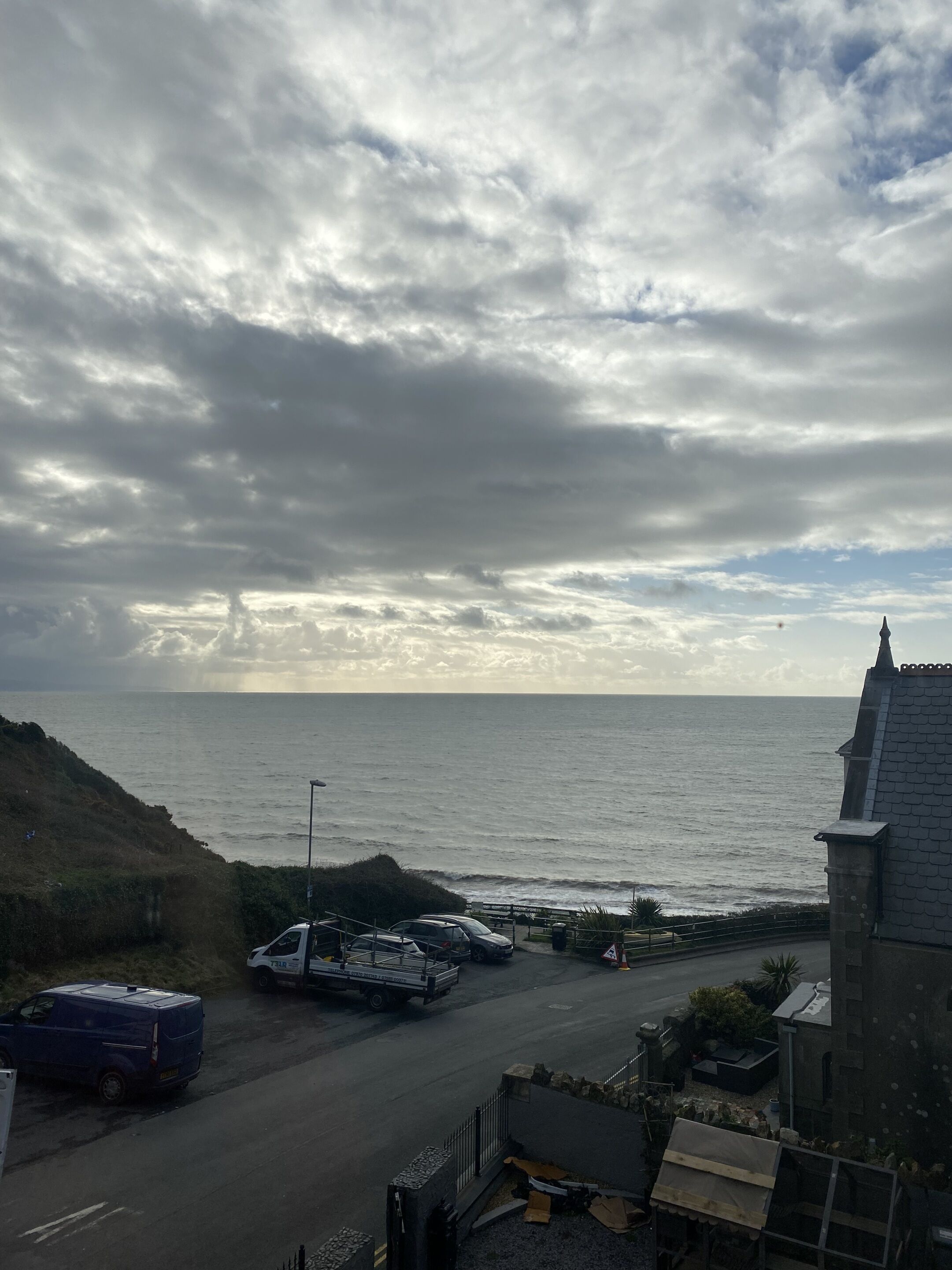 A coastal road with parked vehicles and a building with a pointed roof.