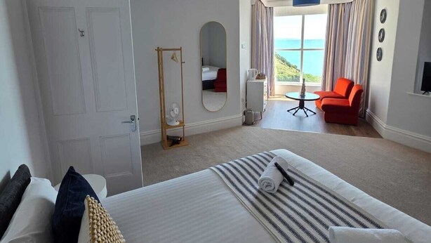 Habitación de hotel con cama, escritorio, una silla, vista al mar y un ventanal grande.