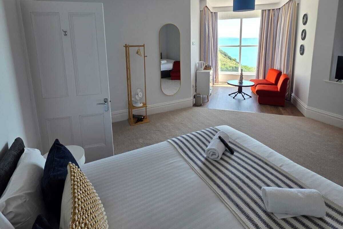 Ein Hotelzimmer mit Bett, Schreibtisch, Stuhl und Meerblick, sowie einem großen Fenster.