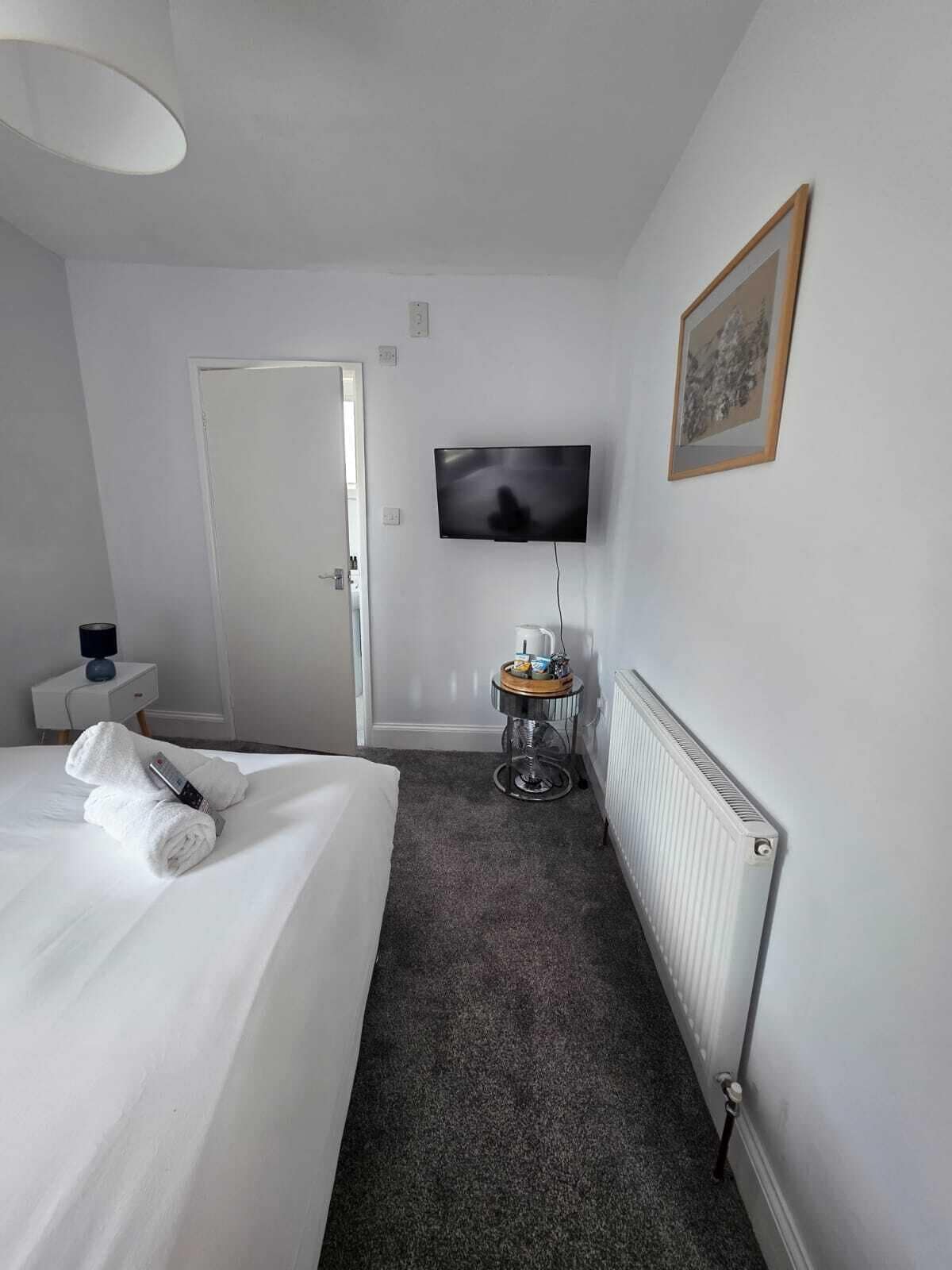 A hotel room with a bed, a television, a radiator, and a small table with a tray.