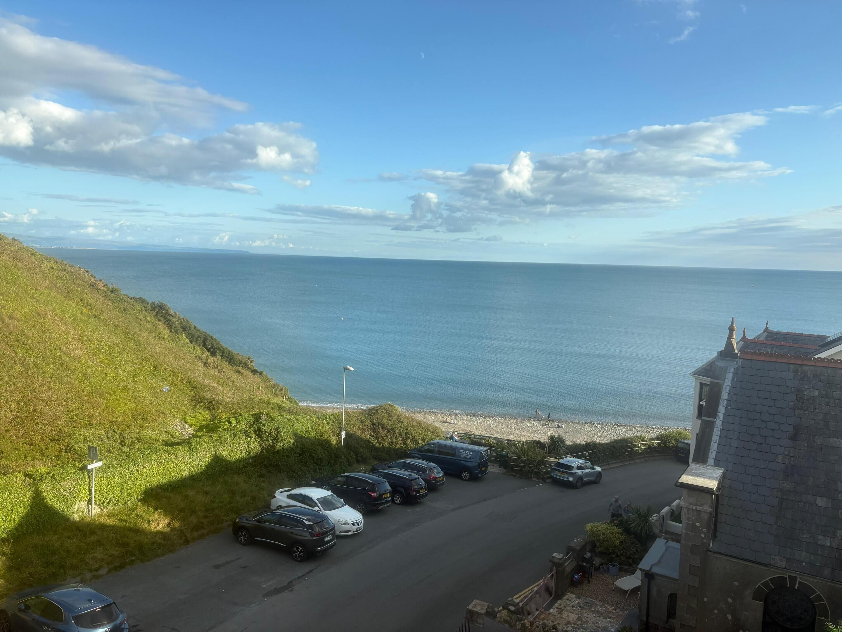 A parking area with cars, a grassy hill, and a view of the sea.