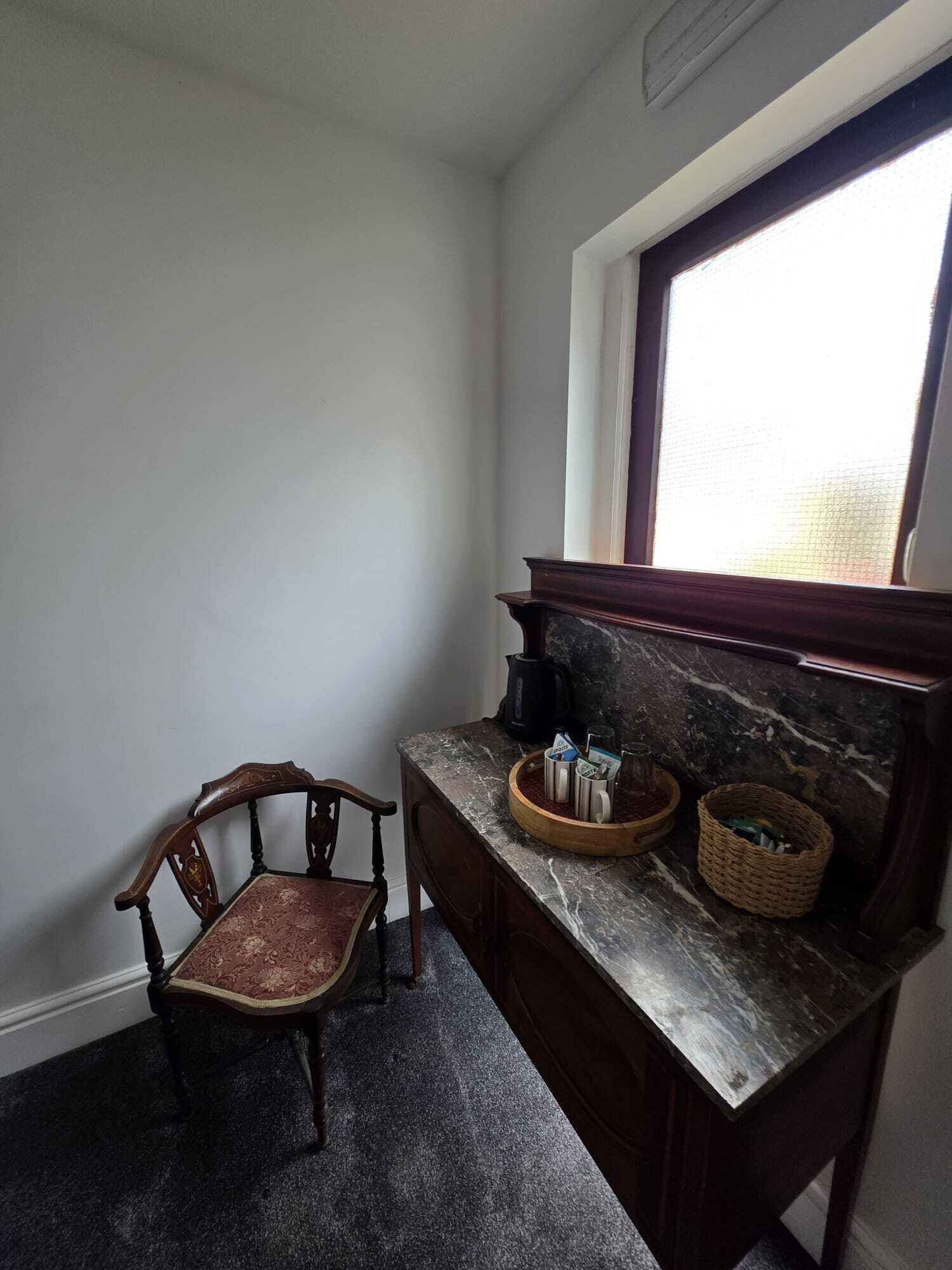 A corner room with a wooden chair, a marble countertop, and a window with blinds.
