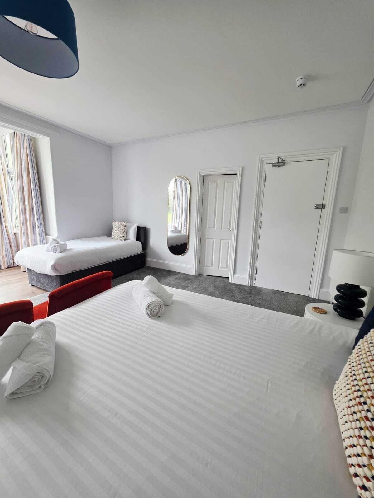 A hotel room with a large bed, a smaller bed, a mirror, a door, and a lamp.