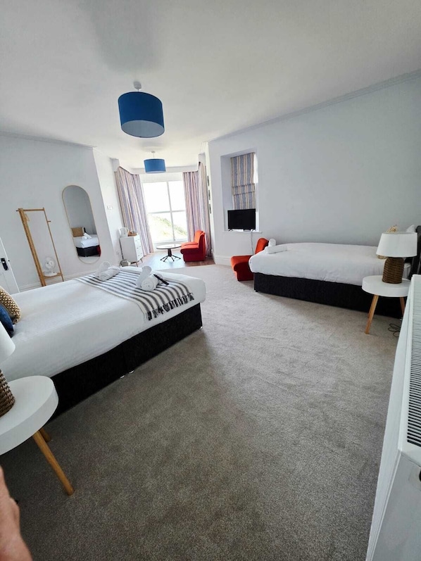 A modern hotel room with two beds, a large window, a flat-screen TV, and a small round table. - Marine Hotel (Criccieth)
