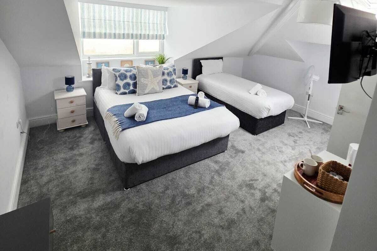 Ein modernes, gut beleuchtetes Schlafzimmer mit einem großen Bett, einem kleineren Bett und einem Fernseher.