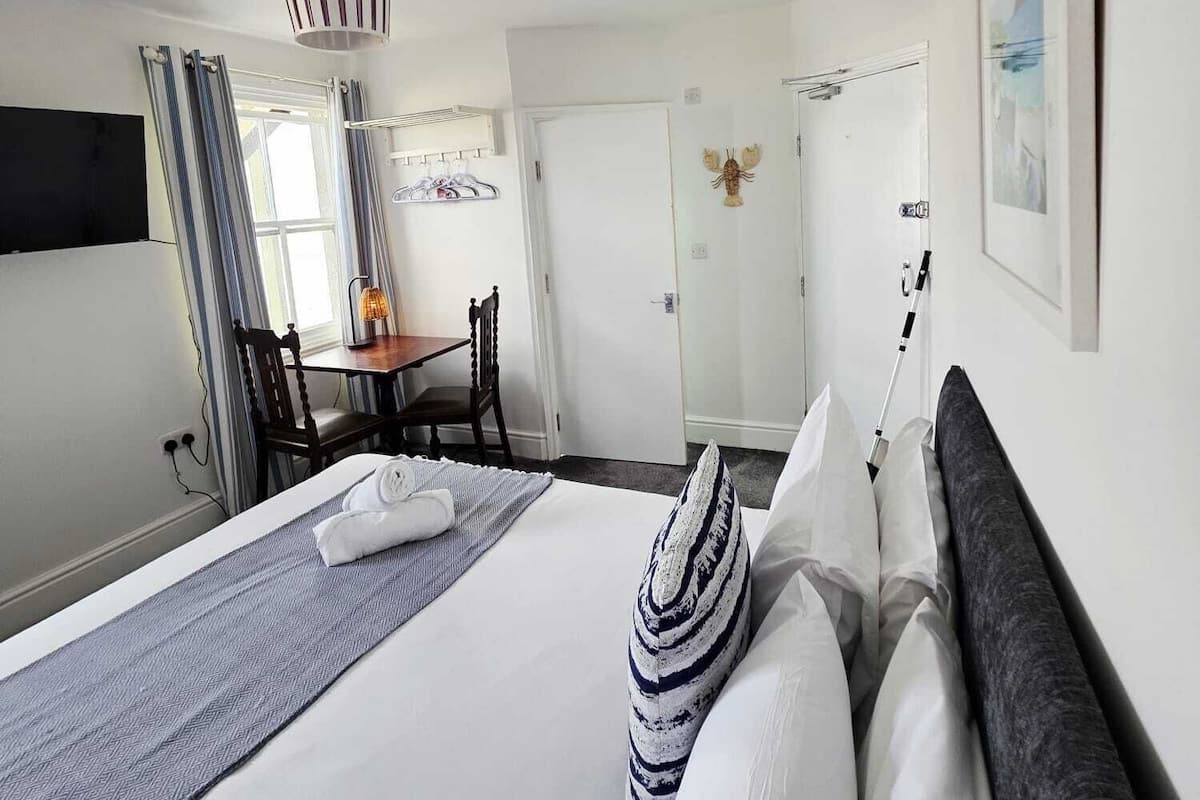 Ein Hotelzimmer mit einem großen Bett, einem Schreibtisch und einem Stuhl. Es gibt ein Fenster mit Vorhängen, eine Wandheizung und ein gerahmtes Bild an der Wand.