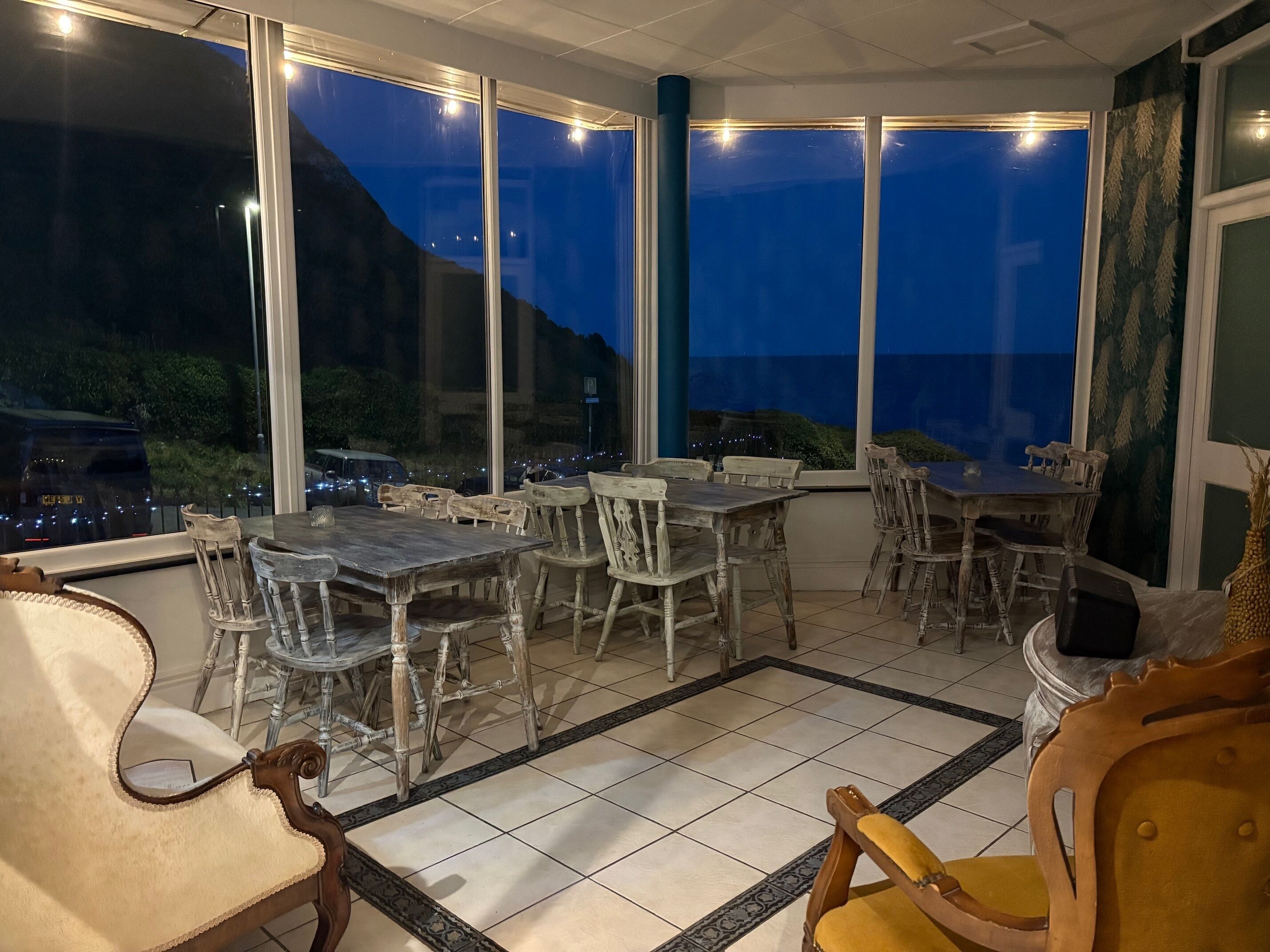 A dining area with tables and chairs, large windows, and a view of the cityscape at night.