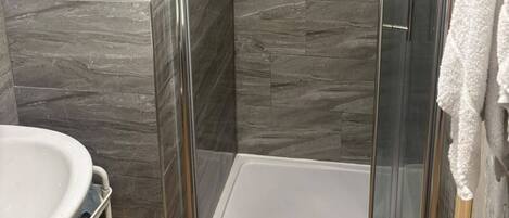 A shower stall with a glass door, a white sink with a yellow towel, and a white towel hanging on the wall.