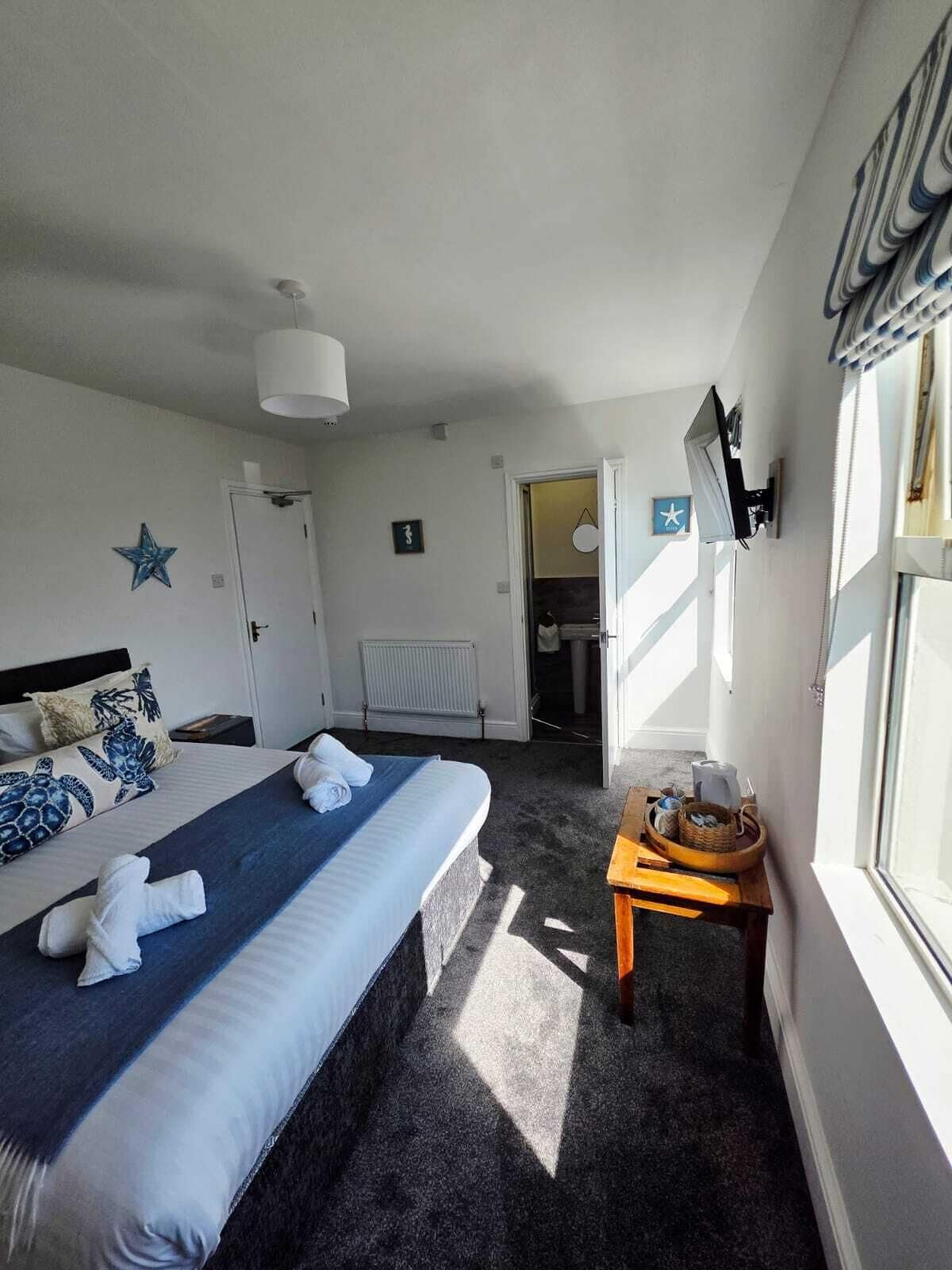 Une chambre d’hôtel comprenant un lit, une table de chevet avec un panier, un radiateur, une décoration en forme d’étoile et une porte donnant sur une salle de bain.