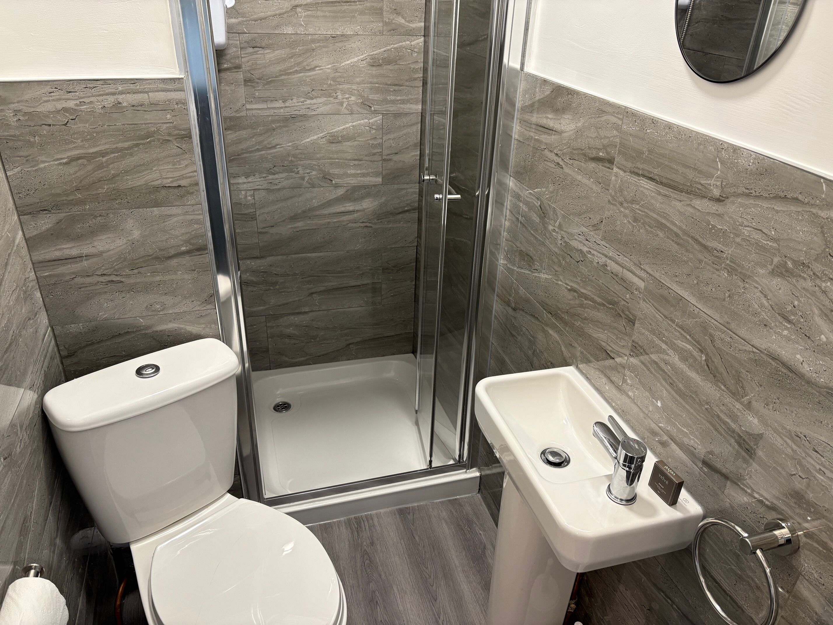 Een badkamer met toilet, een douche met glazen deur en een wastafel met spiegel.