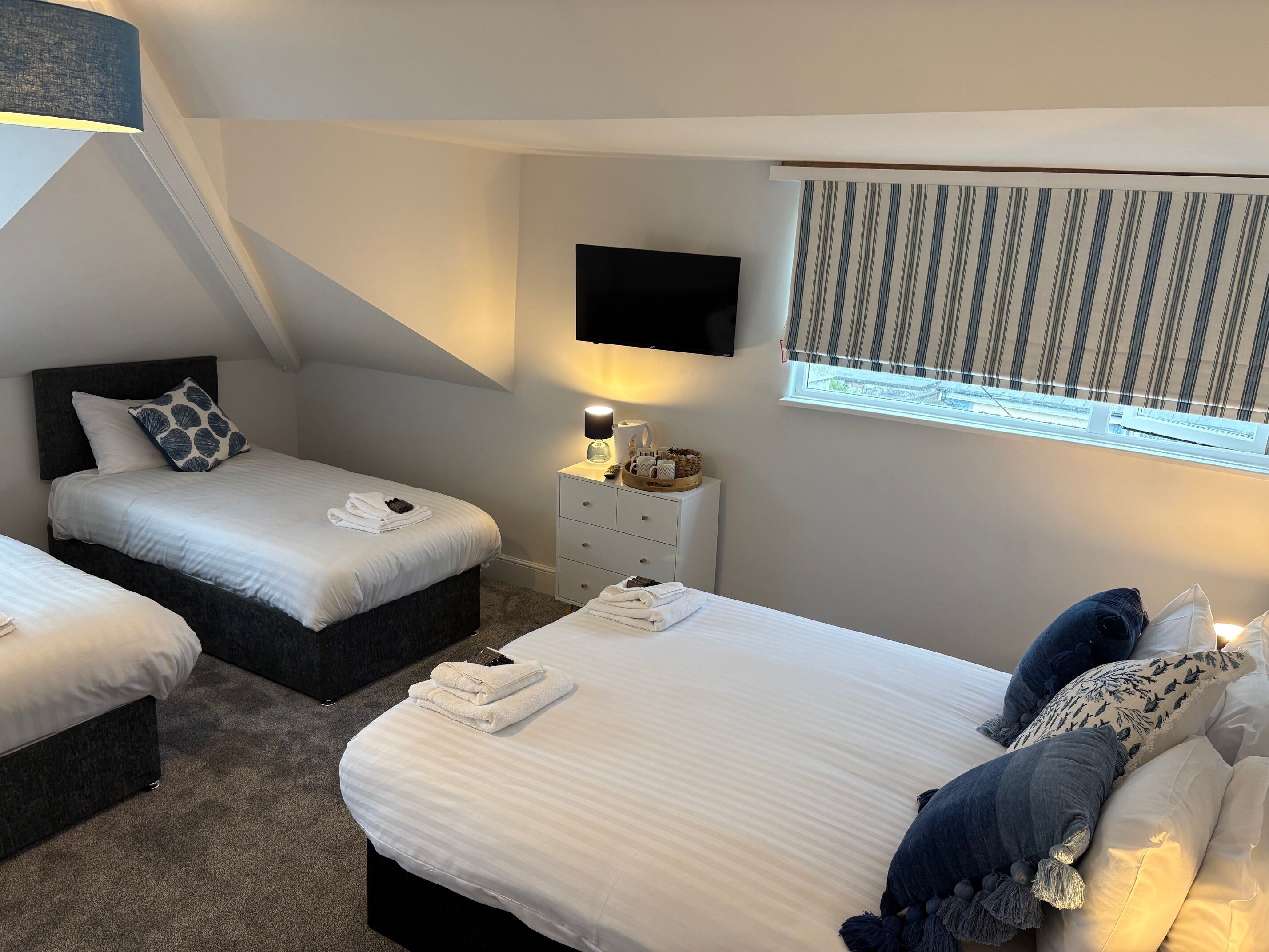 Une chambre d’hôtel avec deux lits, une télévision, une table de chevet avec une lampe et une fenêtre avec des rideaux à rayures.