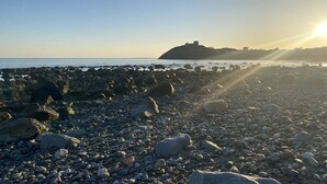 Una playa rocosa con una construcción que se asemeja a un castillo a lo lejos.