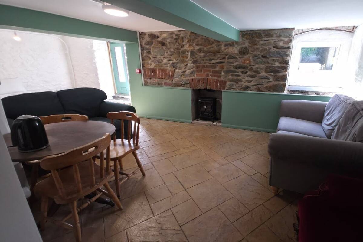 Ein Wohnzimmer mit Kamin aus Stein, einem Esstisch mit Stühlen und einer Couch.