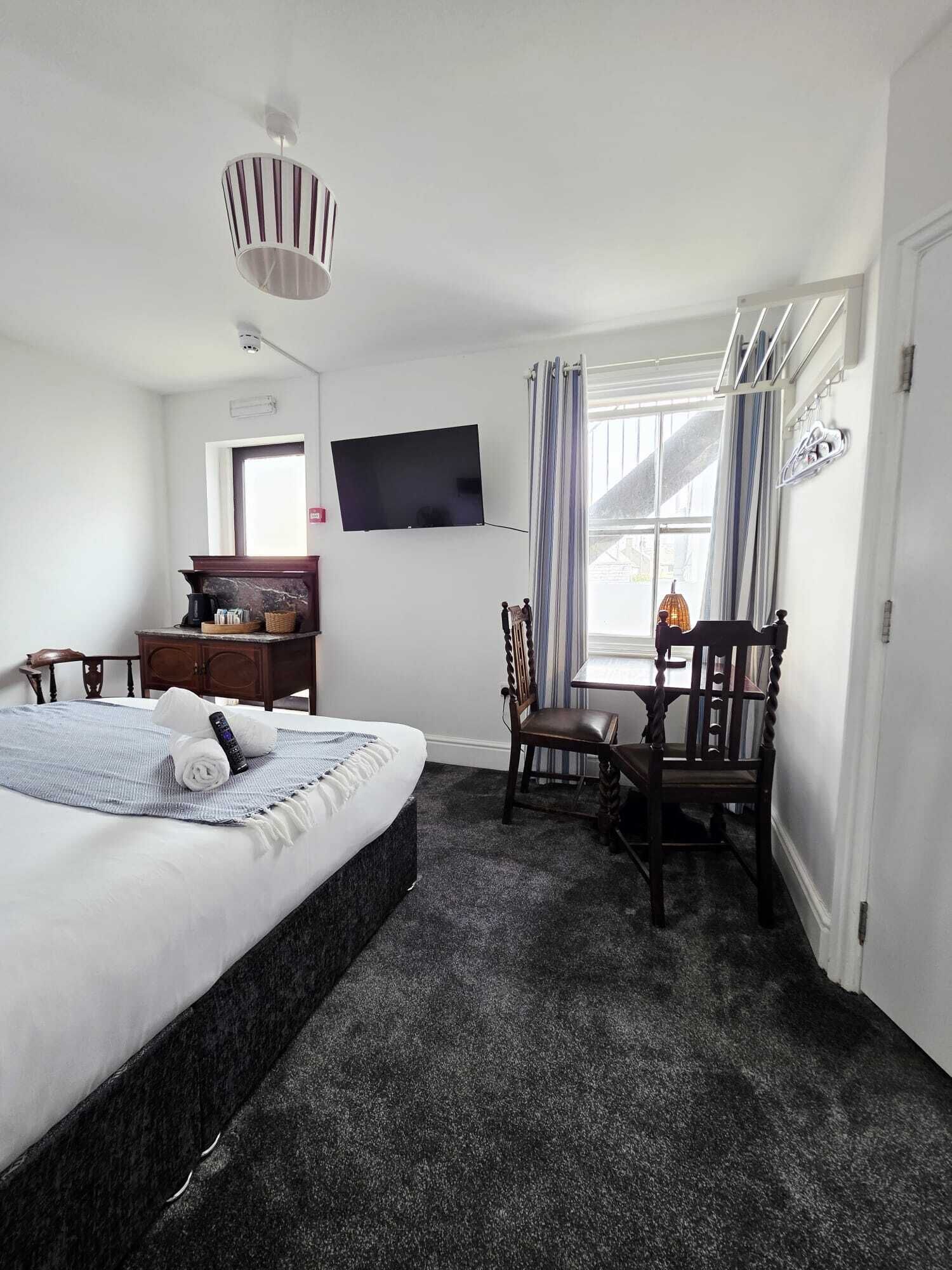 Una habitación de hotel con cama, escritorio, silla, televisor y ventana con cortinas.