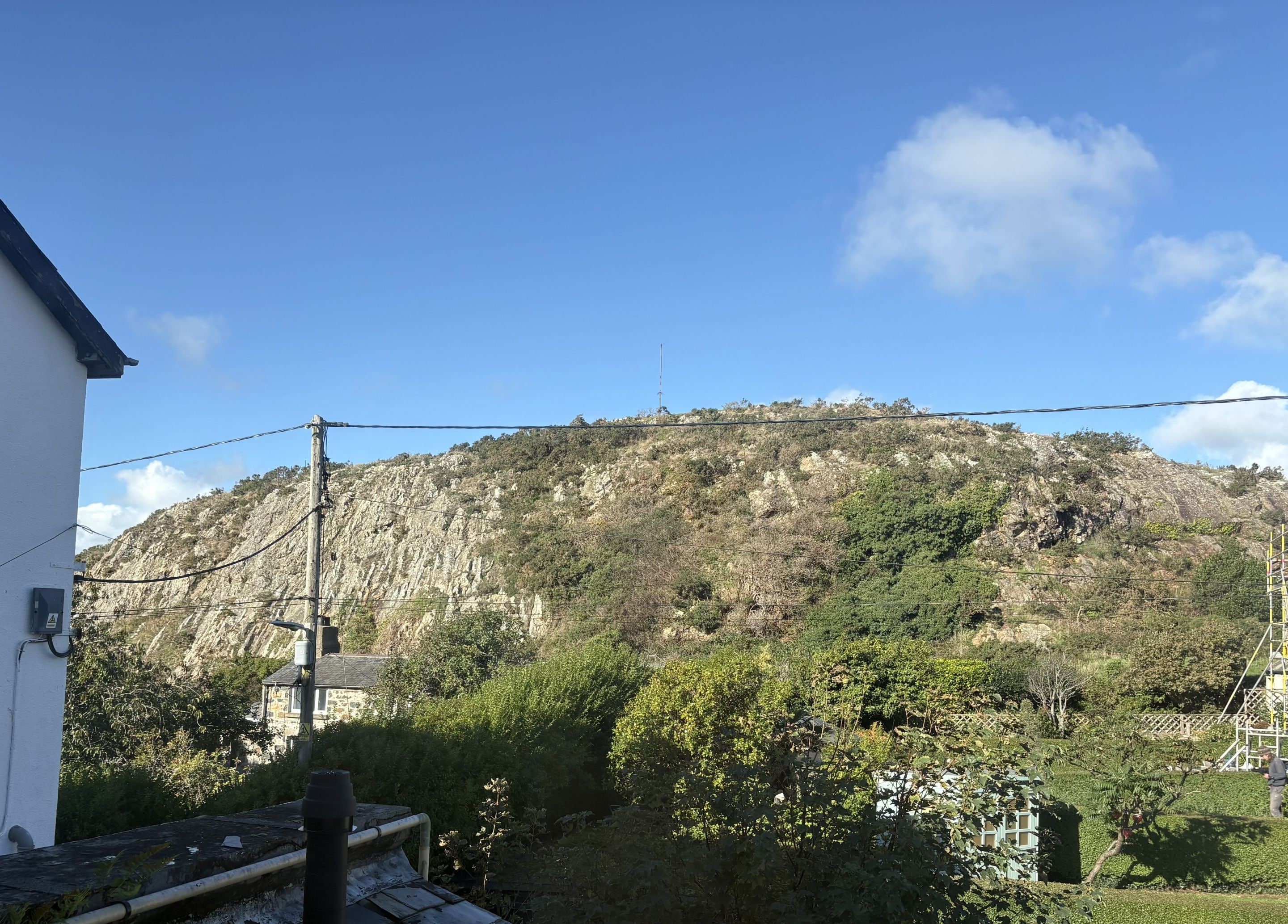 A view of a hillside with a building in the foreground, a clear sky, and a rocky terrain.