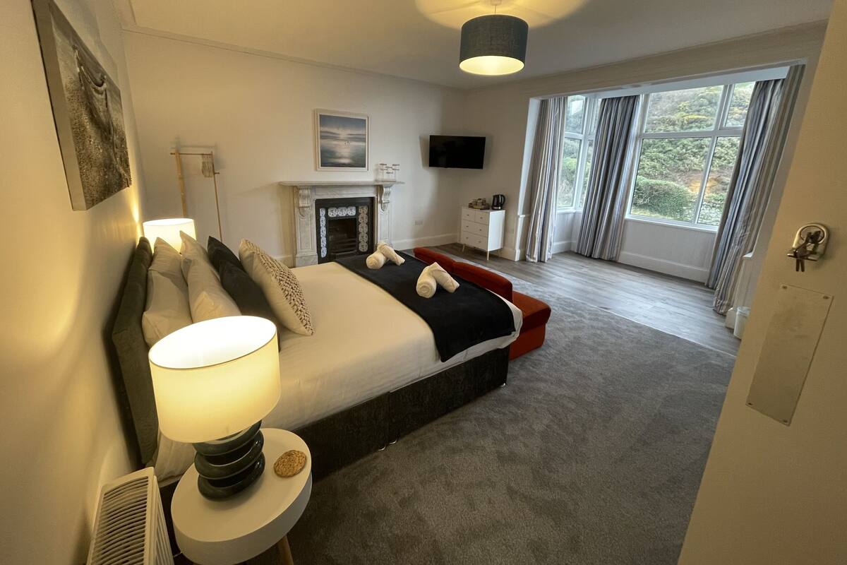 Ein modernes Hotelzimmer mit einem großen Bett, einem Kamin, einem Fernseher und Blick ins Freie.