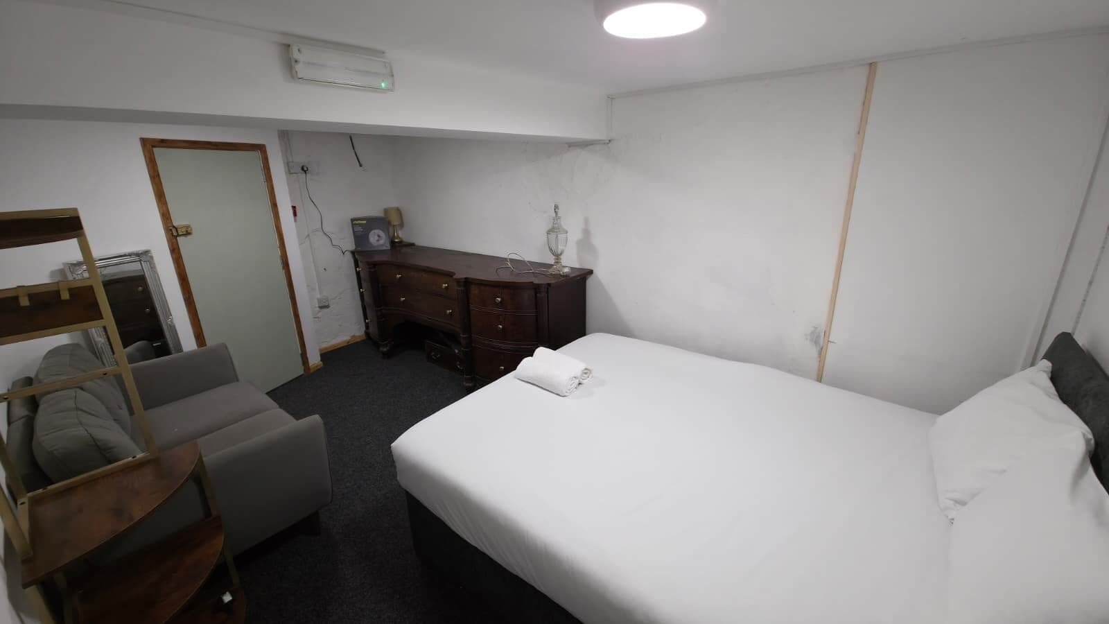 Una habitación de hotel con cama, escritorio, silla, armario y un pequeño rincón de descanso.