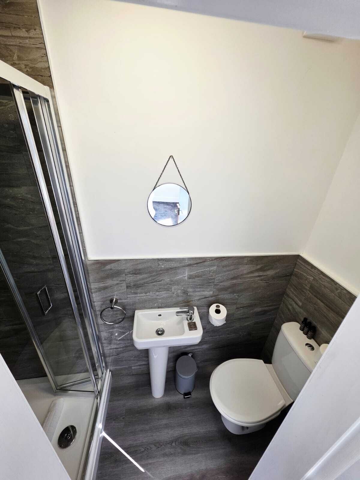 A compact bathroom with a glass shower enclosure, a pedestal sink, a toilet, and a wall-mounted mirror.