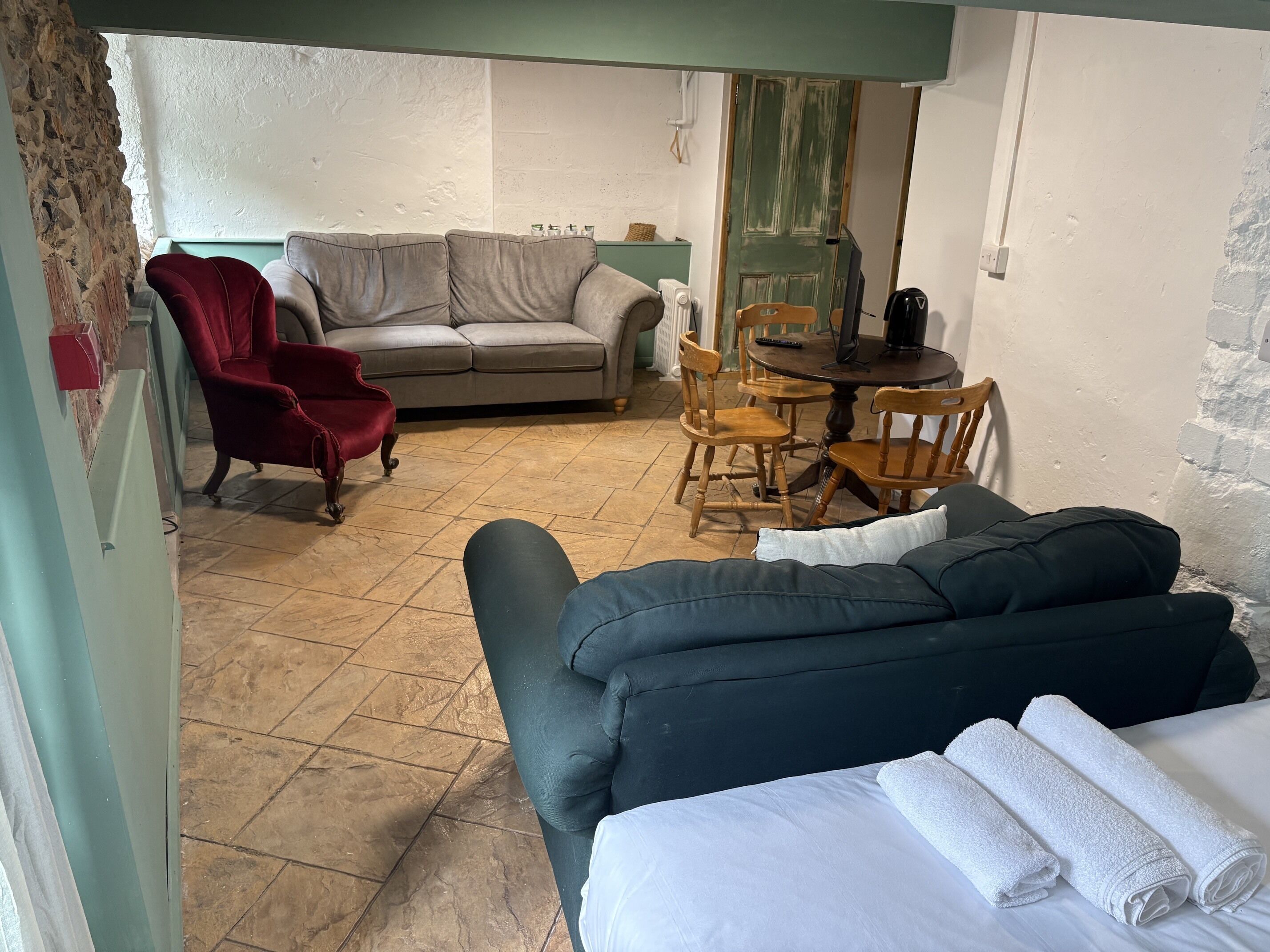 A room with a sofa, a chair, a dining table with chairs, and a bed with towels.