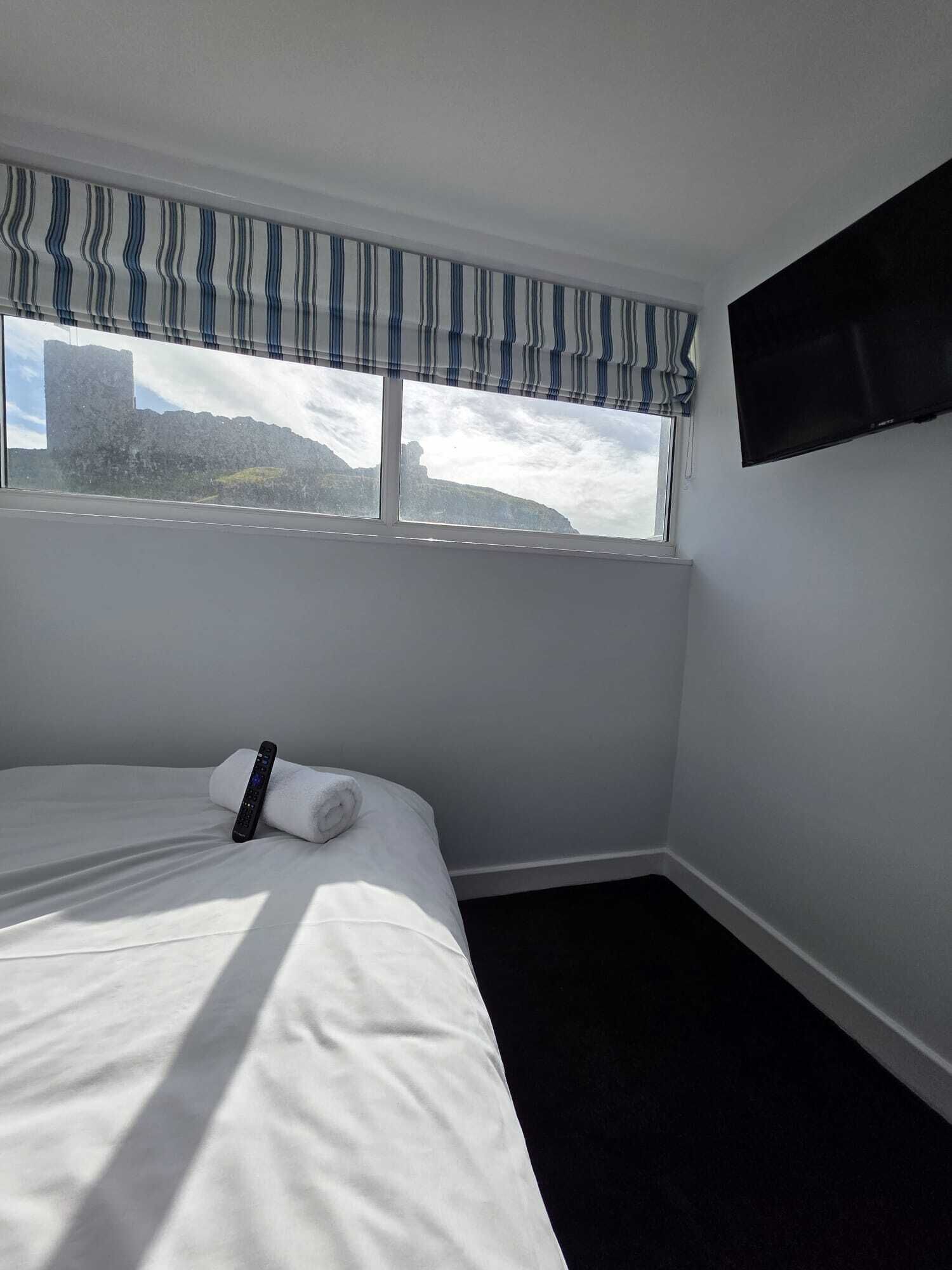 A hotel room with a bed, a TV mounted on the wall, and a window with a view of a mountain and a cityscape.