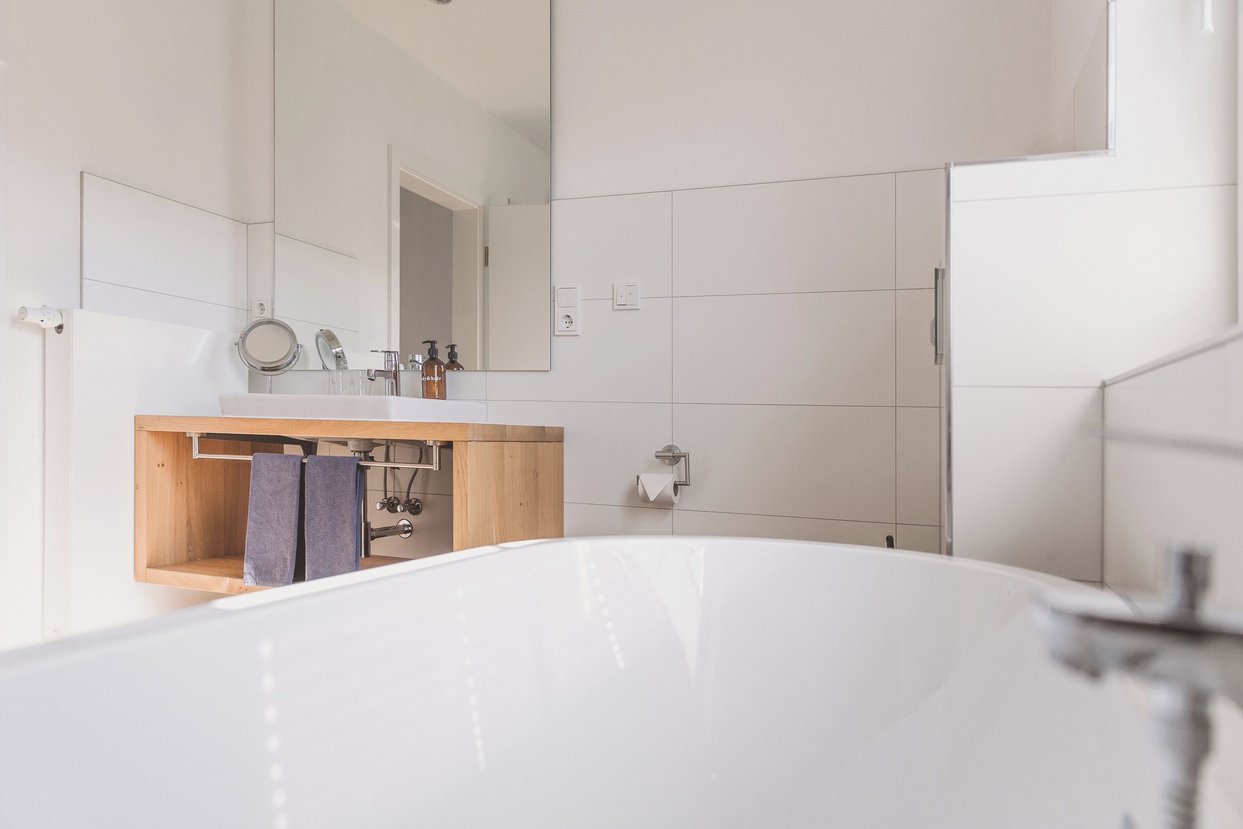 A modern bathroom with a freestanding bathtub, a wooden vanity, a mirror, and a towel rack.