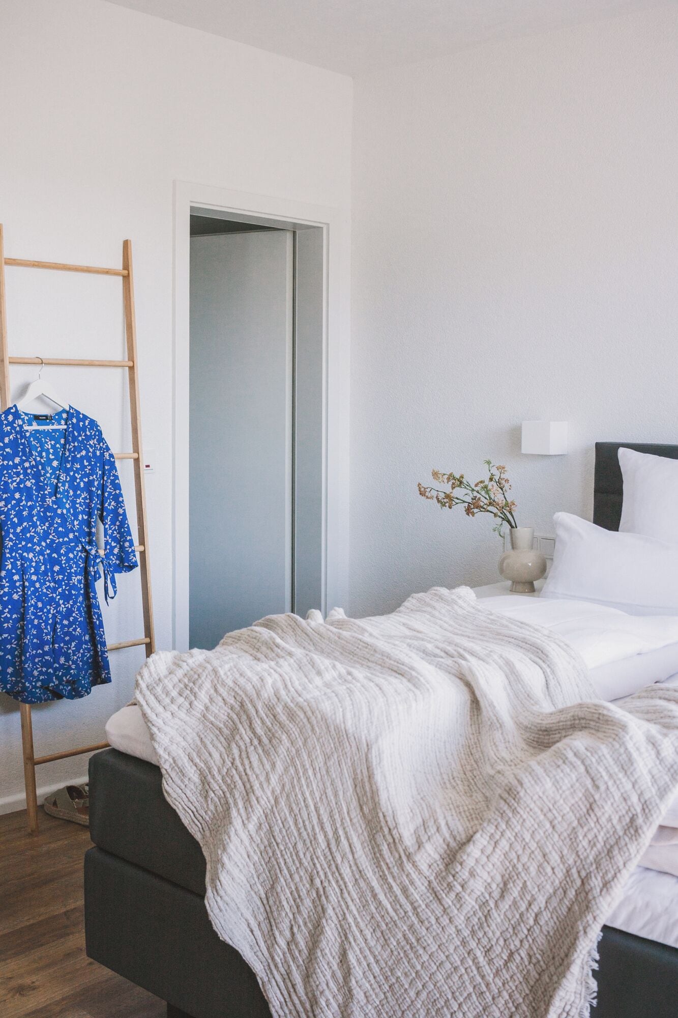 A bedroom with a bed, a wardrobe, a mirror, and a small table with a vase.