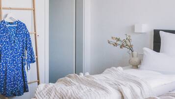 A bedroom with a bed, a wardrobe, a mirror, and a small table with a vase.