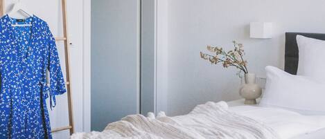 A bedroom with a bed, a wardrobe, a mirror, and a small table with a vase.
