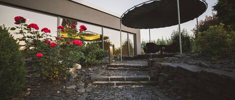 A modern outdoor patio area with a stone pathway leading to a seating area under a large umbrella.