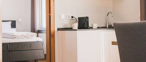 Una habitación de hotel moderna con una cama, una kitchenette con cafetera y una mesa de comedor.