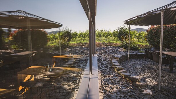 An outdoor seating area with tables and umbrellas, surrounded by a rocky landscape and greenery. - Weingut Gehlen-Cornelius (Brauneberg)
