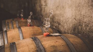 Wooden barrels with glassware on top, likely used for aging wine, in a dimly lit cellar.